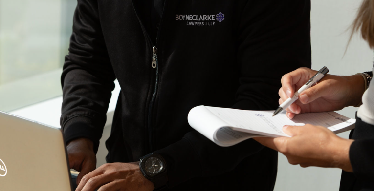 Two BOYNECLARKE team members collaborate, one working on a laptop while the other reviews notes on a clipboard.