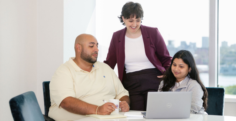 Three BOYNECLARKE colleagues meet around a laptop, smiling and talking during a discussion.